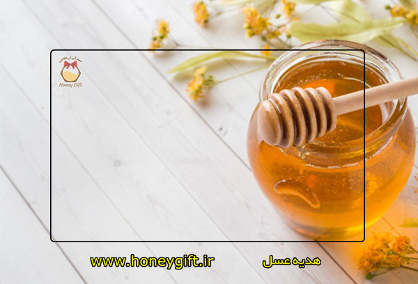 قاشق چوبی عسل روی درب ظرف شیشه ای و تعدادی گل