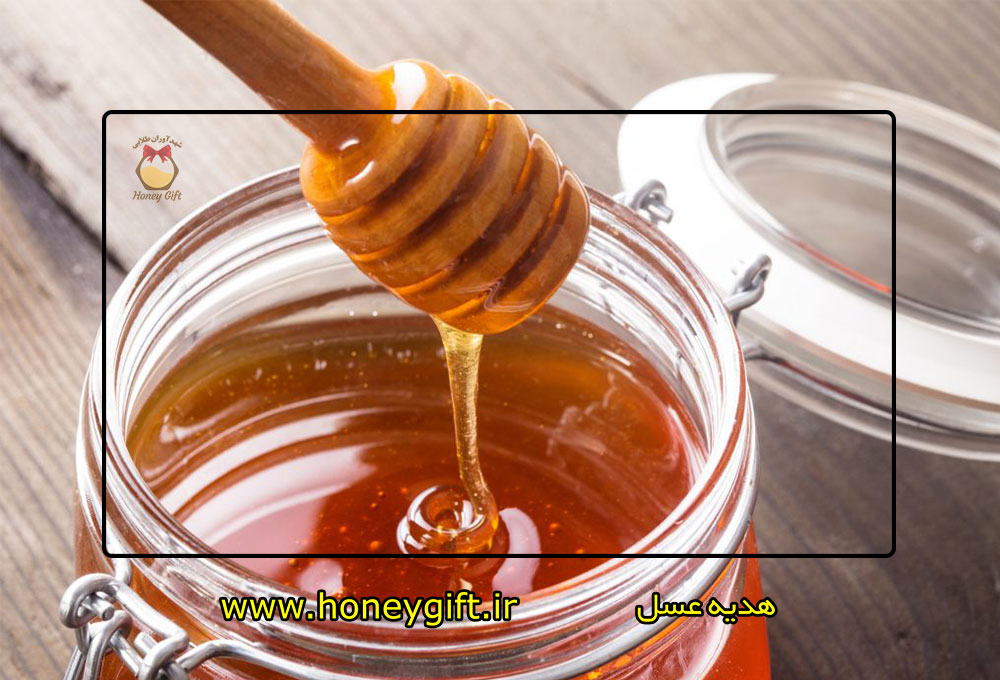 ریختن عسل با قاشق داخل ظرف درب دار روی میز چوبی