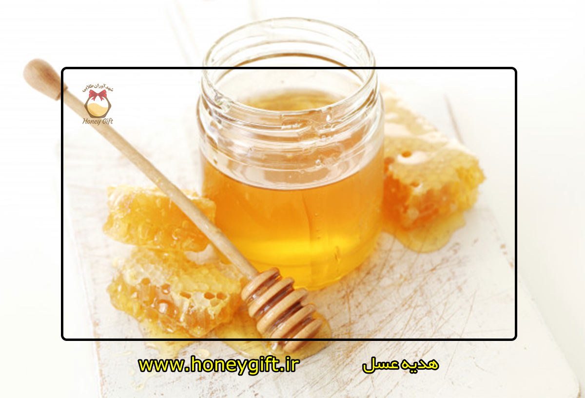 ظرف عسل در کنار موم و قاشق روی میز چوبی
